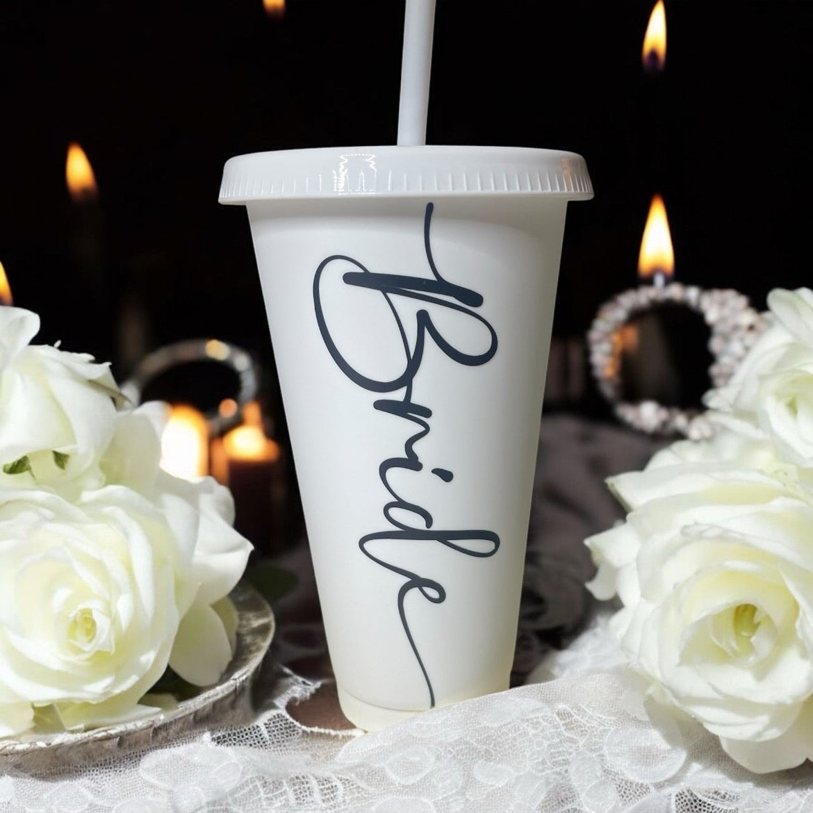 White cup with 'Bride' text, white roses, and blurred candles in the background