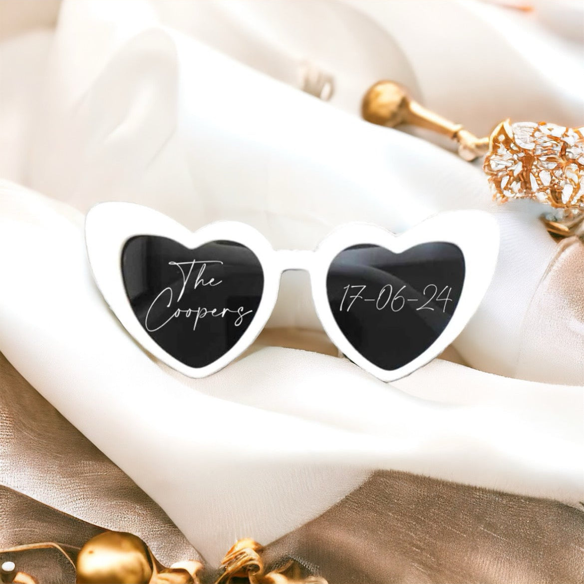 Heart-shaped sunglasses with personalized engraving on a white fabric background