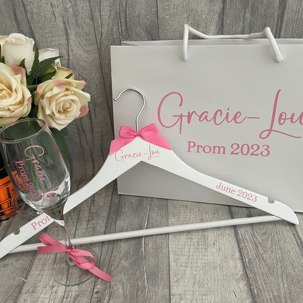 Prom-themed items including a glass, hanger, and gift bag with 'Gracie Lou Prom 2023' text on a wooden surface.