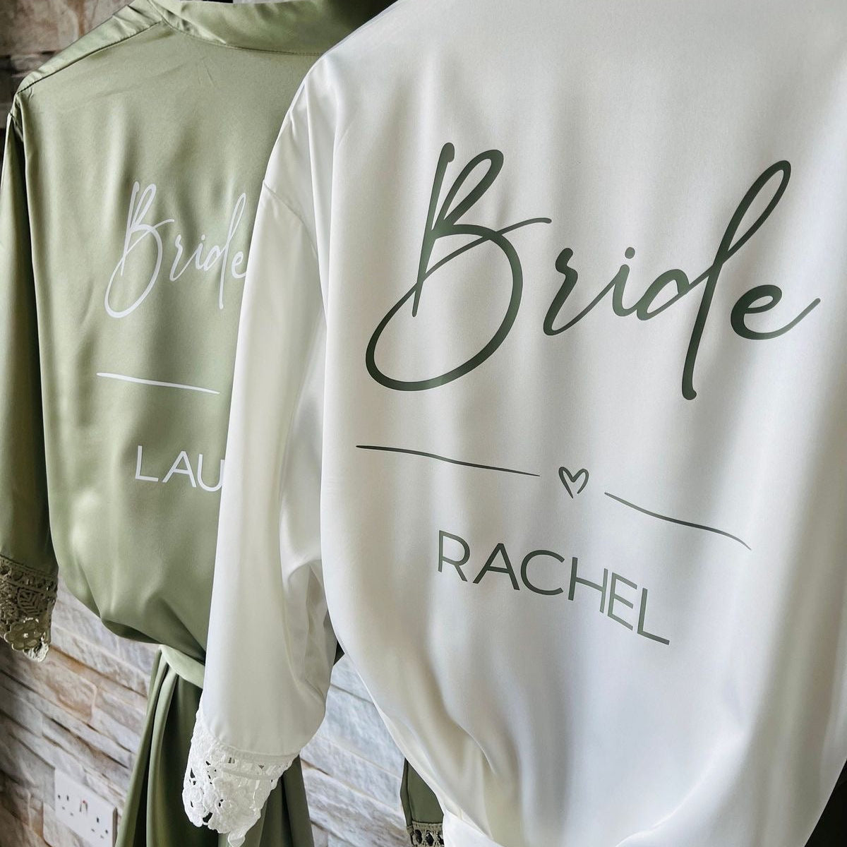 Two sweatshirts, one green and one white, with 'Bride' and 'LAU RACHEL' text on hangers against a stone wall.