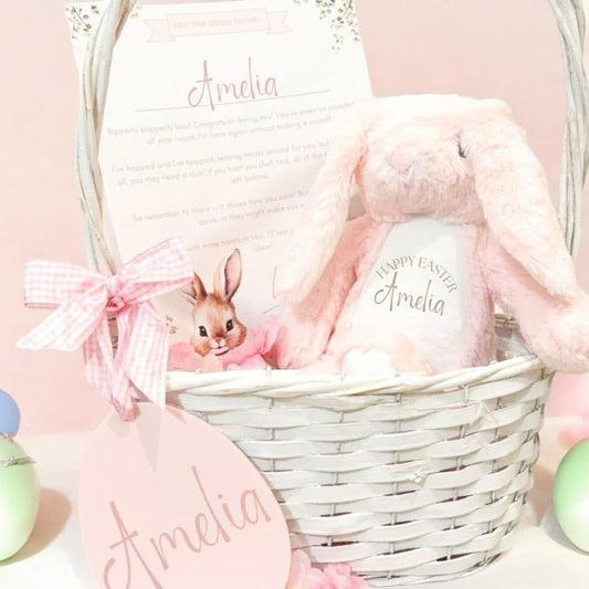 Baby gift basket with plush toys and personalized items on a light pink background