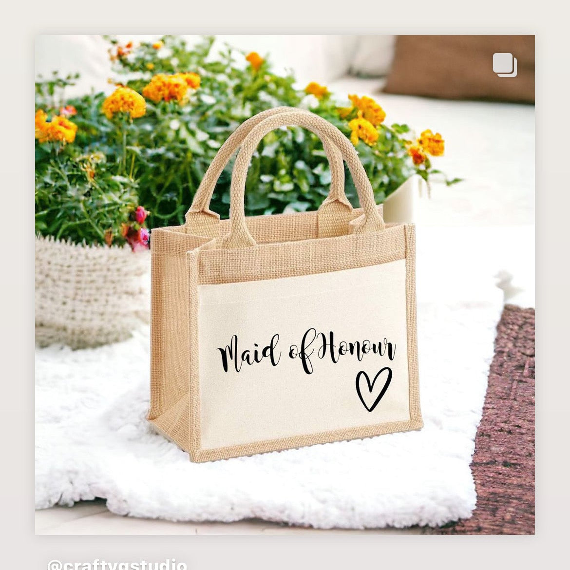 Jute bag with 'Maid of Honour' text on a white surface with flowers in the background
