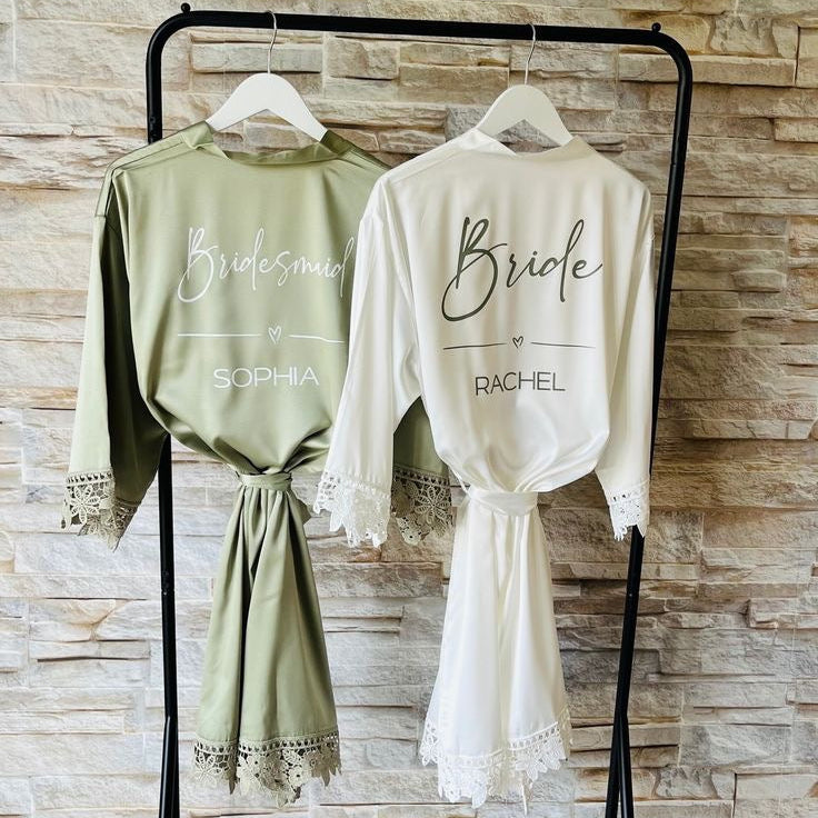 Two robes, one green and one white, hanging on a rack with personalized names on a stone wall background.