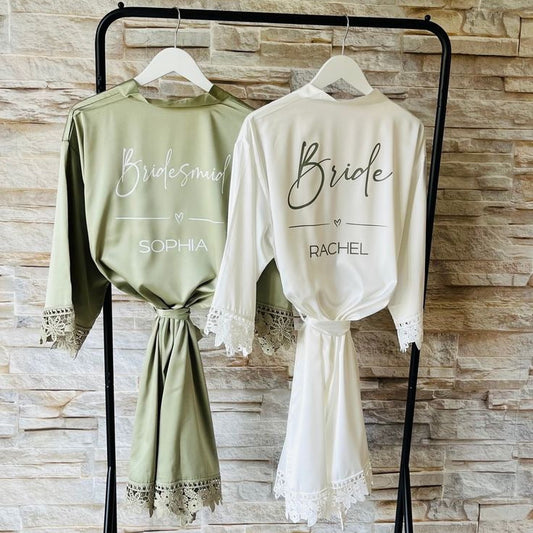 Two robes, one green and one white, hanging on a rack with personalized names on a stone wall background.