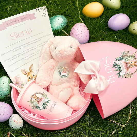 Pink Easter basket with plush bunny, bottle, and personalized note on grass with colorful eggs.