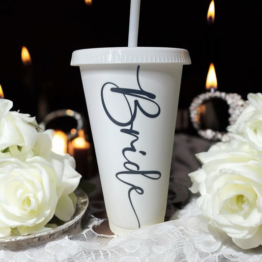 White cup with 'Bride' text, white roses, and blurred candles in the background