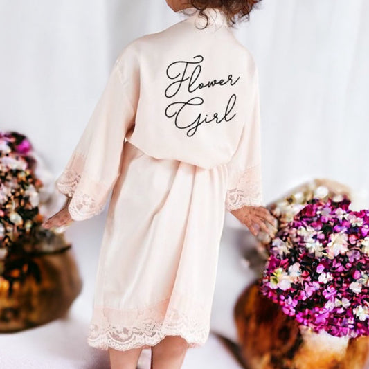 Young girl in a 'Flower Girl' dress standing between floral arrangements.