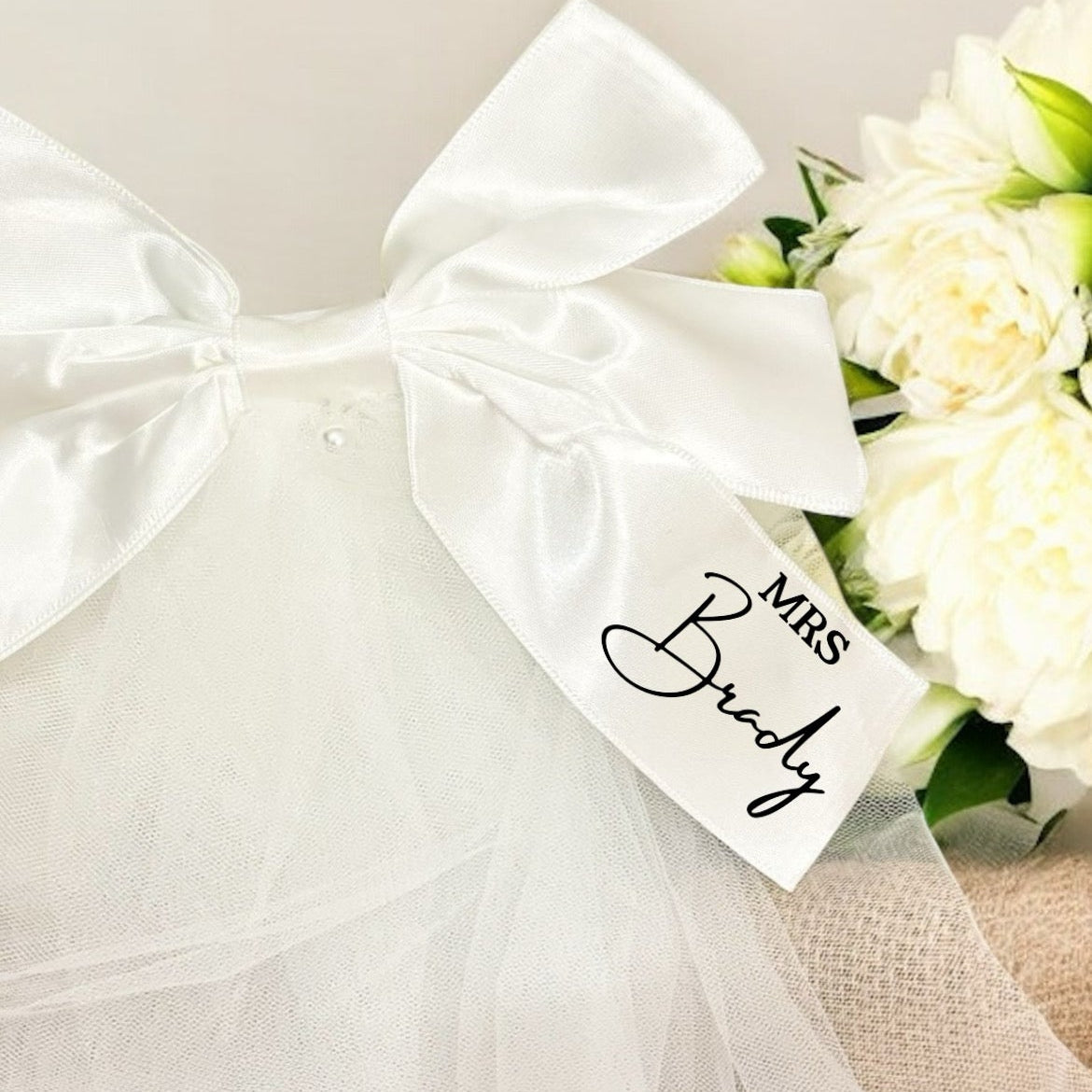 White veil with 'Mrs. Brady' inscription and bouquet of flowers on a light background