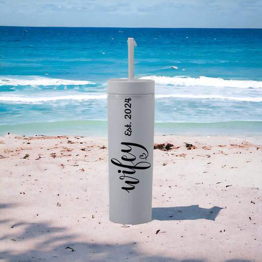 White tumbler with 'wifey' and 'Eck 2024' text on a beach with ocean in the background