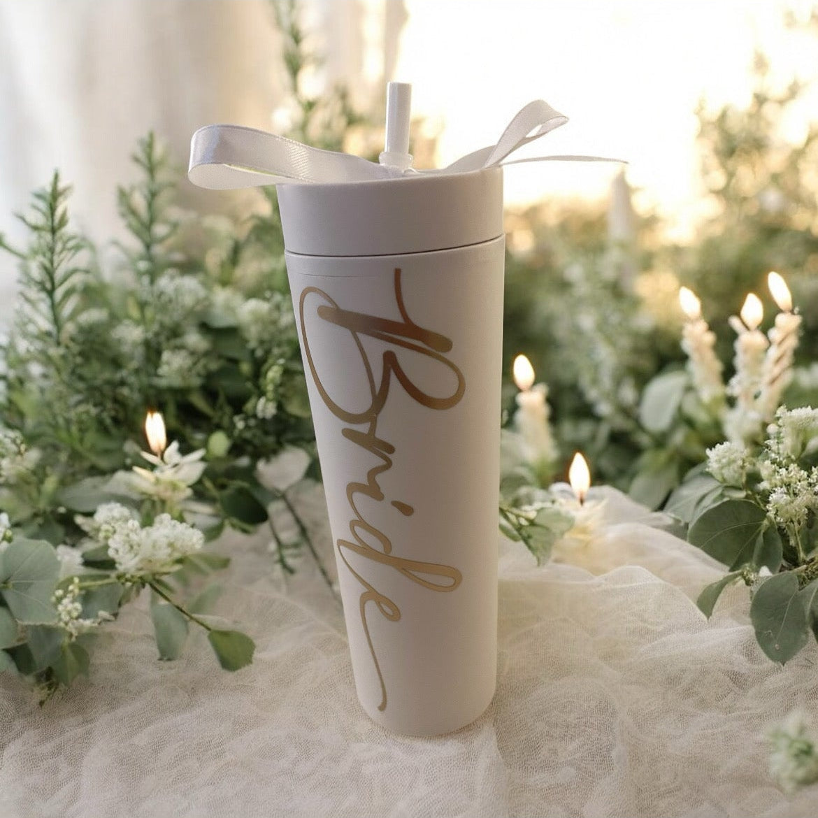 White tumbler with 'Bride' text on a decorative table with greenery and candles. 