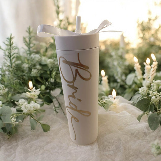 White tumbler with 'Bride' text on a decorative table with greenery and candles. 