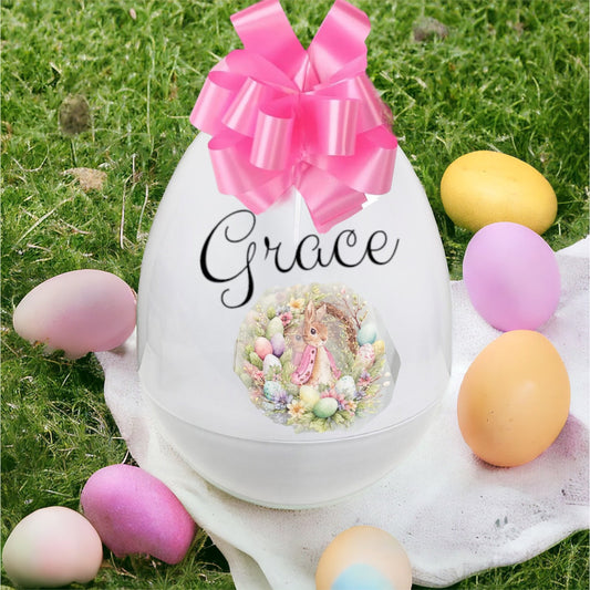 Decorative Easter egg with a pink bow and personalized name on grass with colorful eggs.
