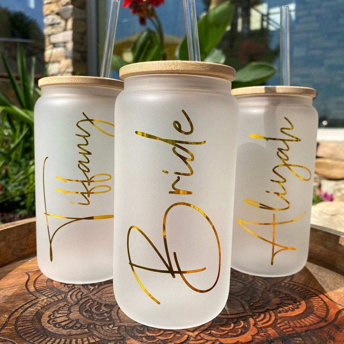 Three frosted jars with gold names on a wooden surface outdoors