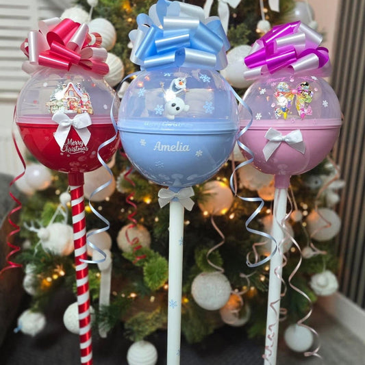 Decorative lollipops with colorful bows and names in front of a Christmas tree.